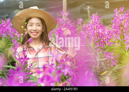 Les jeunes jardiniers femme porter une chemise à carreaux et portez un chapeau. Mains tenant ciseaux pour couper les orchidées et sourire. nouvelle génération d'agriculteurs, jardiniers conce Banque D'Images