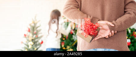 Cadeau de Noël homme tenir derrière le dos de sa petite amie alors qu'elle surprise decorating Christmas Tree dans Chgristmas des fêtes d'accueil. Panoram Banque D'Images