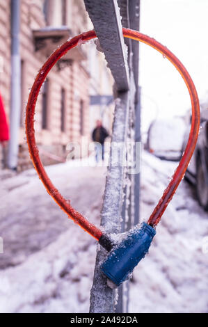 Câble de verrouillage vélo accroché sur la clôture pendant le gel, couvertes de glace, près de la route près de wagons pour prévenir le vol, un voleur ou passer est plus floue dans l Banque D'Images