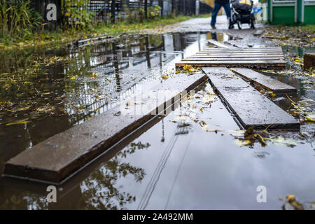 Grande flaque empêche les piétons avec un landau de marcher le long d'un chemin avec parquet à l'automne dans un parc de la ville Banque D'Images