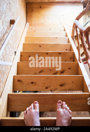 Les jambes d'un homme debout sur la plus haute marche d'un escalier en bois, dans une maison. Banque D'Images