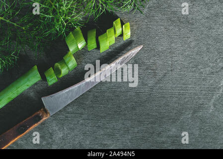 L'oignon et couteau de cuisine sur une planche à découper noire pierre fond. Banque D'Images