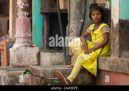 RAGHURAJPUR, INDE, LE 14 JANVIER 2019 : Une jeune Indienne portant une robe jaune est assis dans la rue avec un pied sur le guidon de sa bicycl Banque D'Images