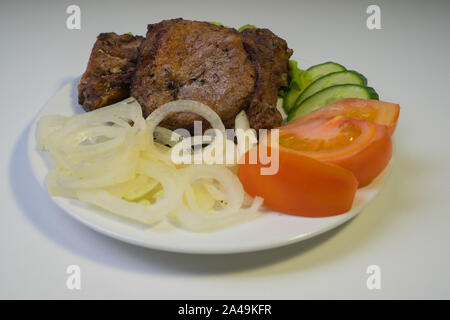 Grillades de viande juteuse sur une plaque blanche avec des oignons, des concombres et des tomates et une salade. Banque D'Images