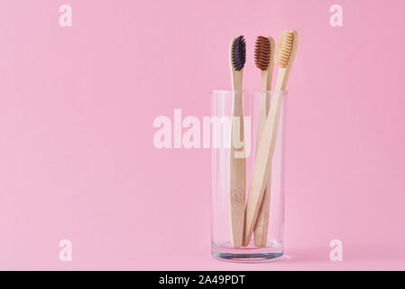 Trois brosses à dents en bambou en bois en verre sur fond rose. Concept d'hygiène dentaire Banque D'Images