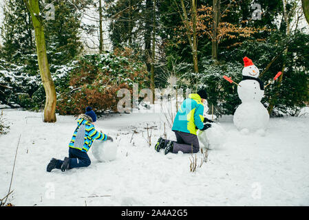 Père avec peu de fils de croisière snowman dans city park Banque D'Images