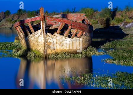 Le cimetière de bateaux de Noirmoutier. Éclairé par les lampes du port, l'épave d'un vieux bateau de pêche en bois échoué sur un lit de verdure se reflète dans la Banque D'Images