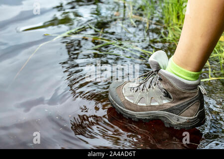 Femme en bottes de randonnée imperméable touristiques promenades à travers l'eau dans les flaques. Close-up. Banque D'Images