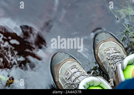 Femme en bottes de randonnée imperméable touristique est debout dans l'eau dans une flaque. Close-up. Banque D'Images