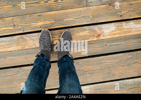 Les jambes des femmes en bottes en daim élégant debout sur un pont de planches de bois par une froide journée d'hiver,. Vue d'en haut. Banque D'Images