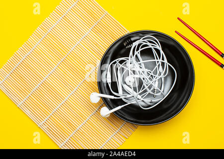 Le casque dans une assiette sur un tapis de bambou et d'un fond jaune, à côté sont de baguettes. Notion de goût musical. Close-up. Banque D'Images