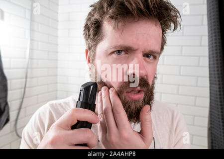 Un jeune homme regarde dans le miroir à sa barbe hirsute hairstyle et épais et qu'il va se faire une coupe à l'aide d'un massicot. Clos Banque D'Images