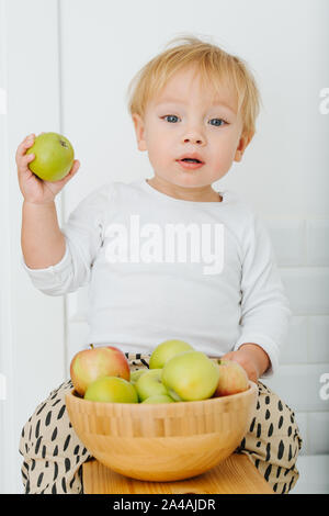 Lly blond bébé garçon est explore, joue avec des pommes de backet. Banque D'Images