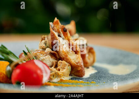 Délicieuses crêpes aux champignons et fromage, servi sur assiette bleue avec sauce blanche et la tomate. Banque D'Images