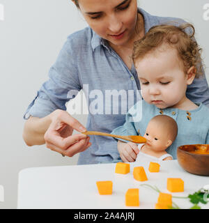 Maman s'alimente plusieurs fille et poupée Banque D'Images