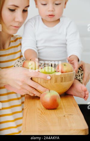 Lly blond bébé garçon est explore, joue avec des pommes de backet. Banque D'Images