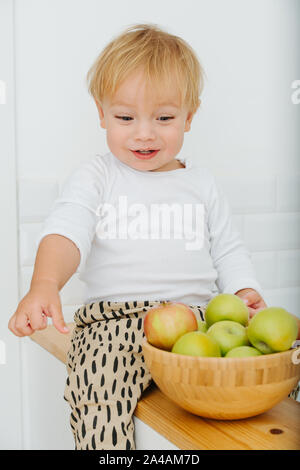 Lly blond bébé garçon est explore, joue avec des pommes de backet. Banque D'Images