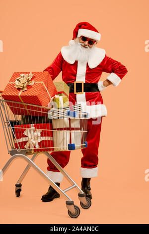 Portrait de senior Saint Nicolas en costume traditionnel préparé des cadeaux pour des enfants heureux. Homme barbu souriant à lunettes avec des boîtes-cadeaux dans votre panier en studio Banque D'Images