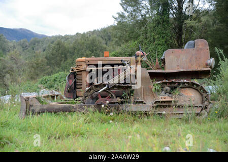 Un bouteur abandonné entre les grands arbres repose sur une colline en Nouvelle Zélande Banque D'Images