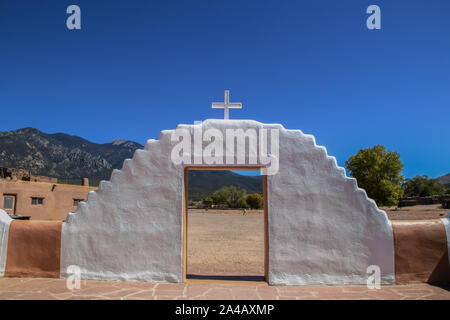 Porte peint surmonté de croix avec montagnes et ciel bleu et l'homme portant seau vue à travers elle à Taos Pueblo au Nouveau-Mexique, États-Unis Banque D'Images