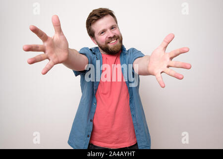 Un bon caractère barbu tire ses mains à l'appareil photo et veut caresser, sourire accueillant un(e) ami(e). Isolé sur fond blanc. Close-u Banque D'Images