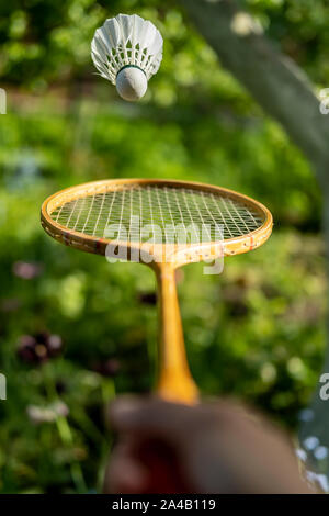 Une main tient une raquette de badminton et de lancer un volant, sur un fond vert, un jour d'été. Close-up. Banque D'Images