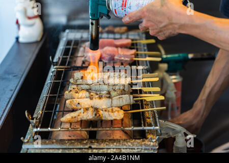 Vue rapprochée des mains d'un cuisinier faisant un steak de poisson sur le gril. Un homme est la cuisine le thon frais bâtons. La flamme de feu est une viande de thon cru de friture Banque D'Images