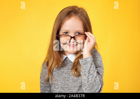 Clever girl écolière avec lunettes. Un enfant dans un chandail gris sur fond jaune. Banque D'Images