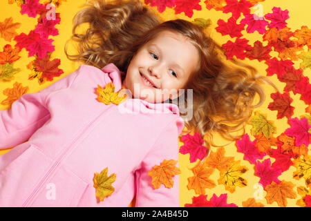 Vue de dessus d'une petite fille joyeuse heureuse étendu sur les feuilles d'automne. Banque D'Images