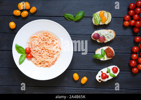 Spaghettis et apéritif bruschettas aux tomates, saumon, fromage crémeux, le basilic, les raisins, le fromage bleu, poire, avocat aux cerises fraîches sur noir woode Banque D'Images