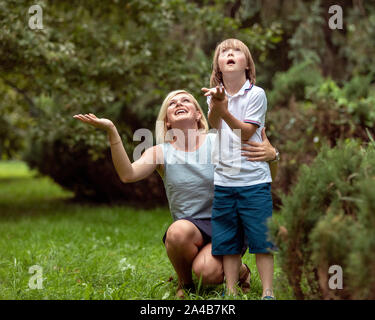 Jeune mère affectueuse et son défi kid sentiment la première pluie gouttes dans un parc d'été Banque D'Images