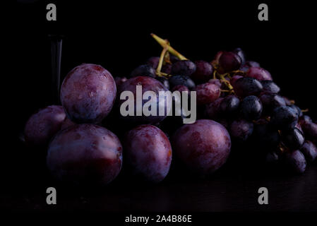 Les prunes et les raisins bleus frais sur un fond réfléchissant noir Banque D'Images