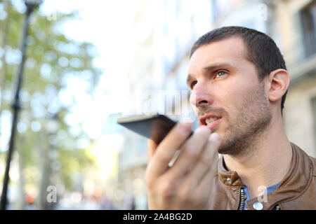 Homme adultes utilisant la reconnaissance vocale sur téléphone mobile pour envoyer un message enregistré dans la rue Banque D'Images