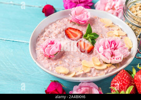 Du jour au lendemain de l'avoine avec des fraises fraîches, amandes et la menthe dans un bol avec des fleurs rose sur table en bois bleu. petit-déjeuner sain. close up Banque D'Images