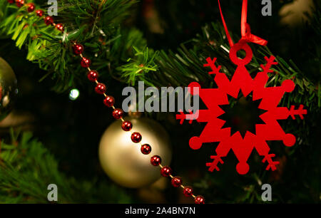 Star ou symbole du flocon de neige de Noël rouge profond, accroché à un arbre de Noël avec une chaîne de petites boules rouge et or boules de Noël dans l'arrière-plan Banque D'Images