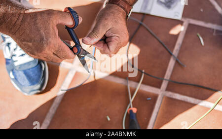 Un homme utilise ses mains et des ciseaux pour dénuder le fil et réaliser des connexions électriques Banque D'Images