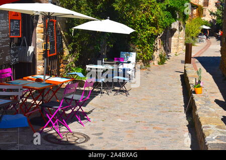 Restaurant bio familial sur une rue pavée de la ville médiévale française. Des tables, chaises, parasols blancs et menus sur un mur de pierre. Banque D'Images