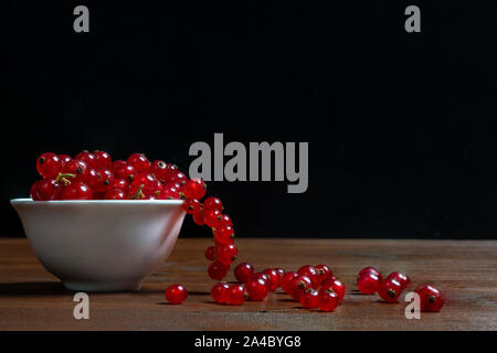 Un bol blanc de cassis avec quelques fruits sur une surface en bois Banque D'Images