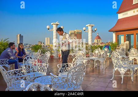 Un serveur sert les clients dans le toit terrasse du restaurant de l'hôtel Godwin, Garden Road, Colaba, Mumbai, le dôme du Taj Mahal Palace Hotel de la b/g (r) Banque D'Images