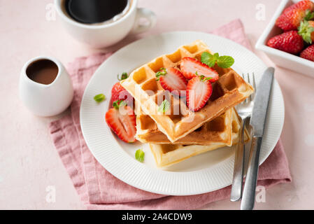 Square des gaufres belges avec des fraises servi avec une tasse de café noir et de sauce au chocolat sur fond rose Banque D'Images