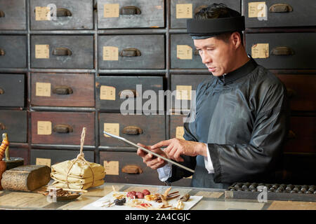 Praticien en médecine traditionnelle chinoise recette suivante sur l'ordinateur tablette lors de l'emballage ingrédients pour client Banque D'Images