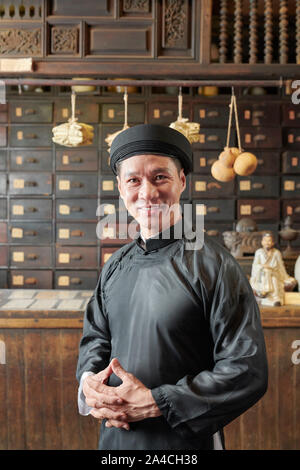 Asian man positive en robe noire traditionnelle et coiffure à l'ancienne pharmacie chinoise de travail Banque D'Images