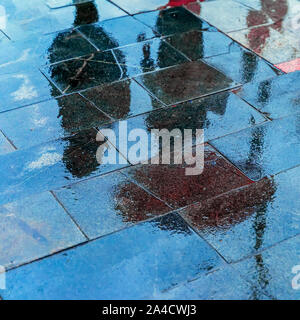 Réflexion floue ombres silhouettes d'une femme sous parapluie et un homme qui marche sous la pluie dans la ville de trottoir, soir de pluie d'automne Banque D'Images