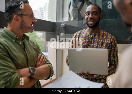 Beau black african businessman holding laptop smiling parler aux collègues portant chemise motif d'inspiration africaine Banque D'Images