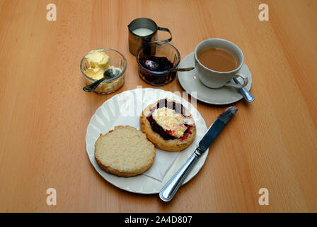 Un thé à la crème traditionnel avec grand scone coupé en deux, avec la confiture de framboises et de crème caillée sur une moitié Banque D'Images