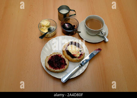 Un thé à la crème traditionnel avec grand scone coupé en deux, avec la confiture de framboises et de crème caillée sur une moitié et la confiture de framboises sur l'autre Banque D'Images