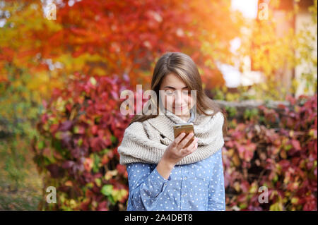 Smart phone automne femme écriture sms sur téléphone mobile à l'automne. Fille de l'automne ayant conversation smartphone à sun flare le feuillage. Portrait de race mixte Banque D'Images