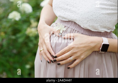 Femme fait un cœur avec ses mains sur sa taille en expansion, son nombril centré. Fleurs et plantes background Banque D'Images