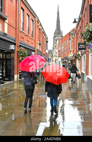 Pleuvoir sur deux femmes marchant le long du temps pluvieux centre ville piétons dans la zone de la rue de shopping sous la pluie parapluie rouge été Durham England UK Banque D'Images