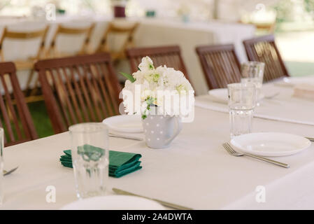 Un petit bouquet de roses blanches et des chrysanthèmes dans une tasse de porcelaine sur la table de dîner Banque D'Images